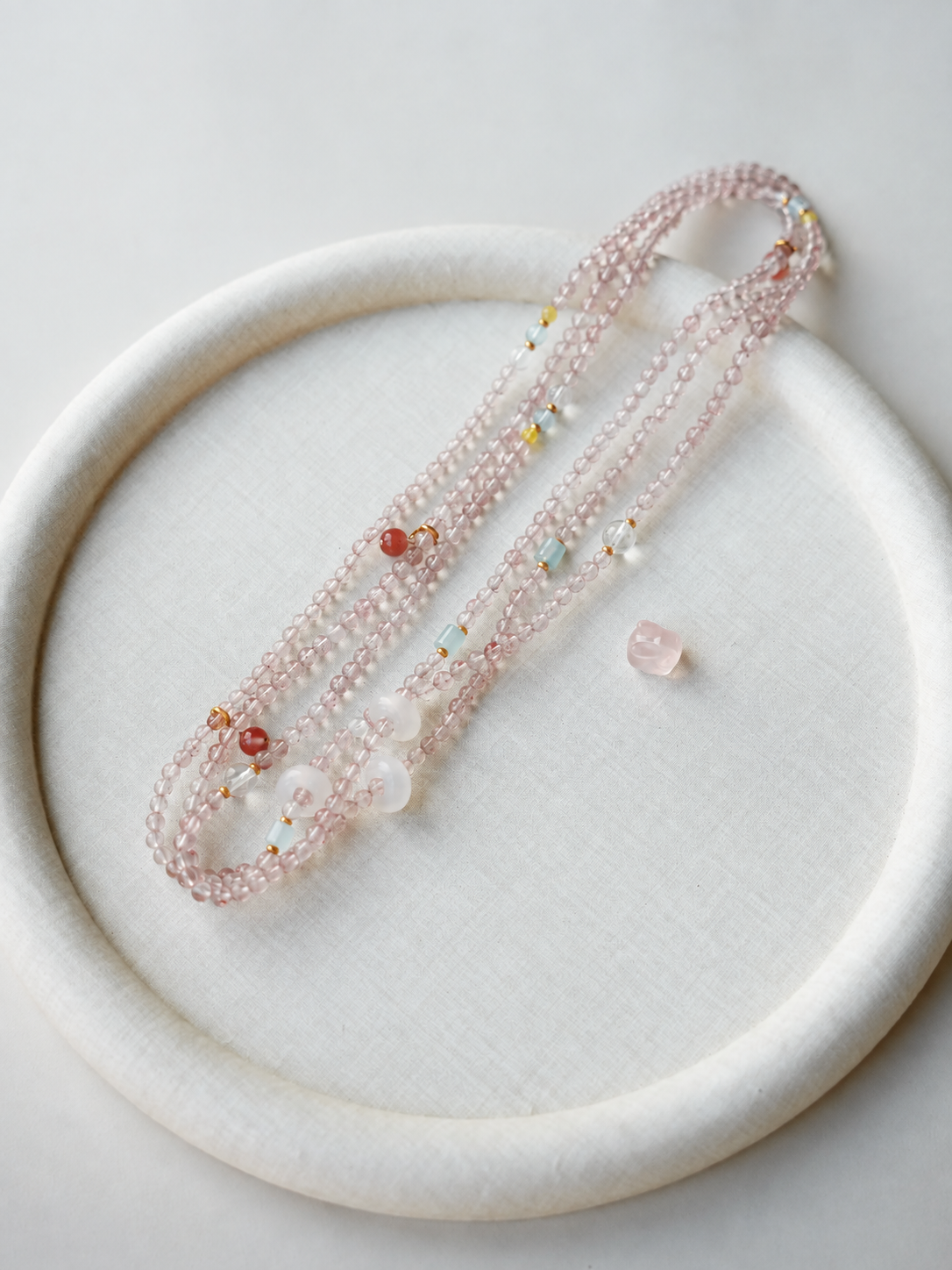 Cloud Weave strawberry quartz strand displayed on a fabric tray