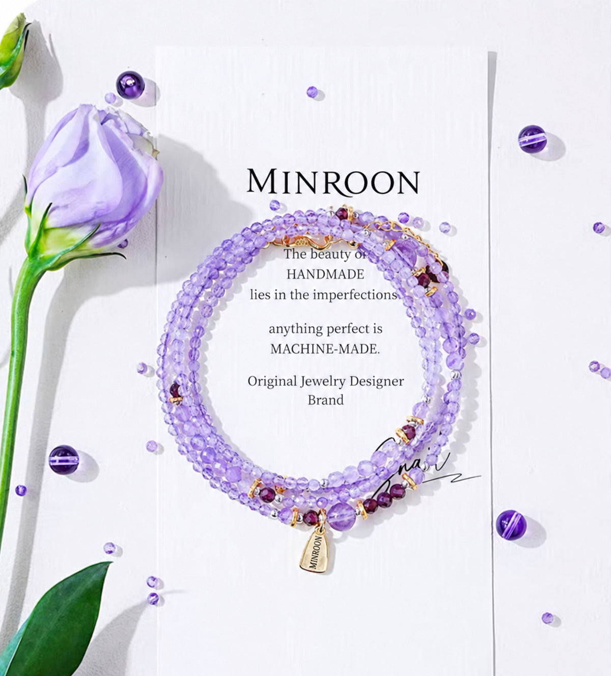MINROON amethyst bracelet laid over a white card beside a flower