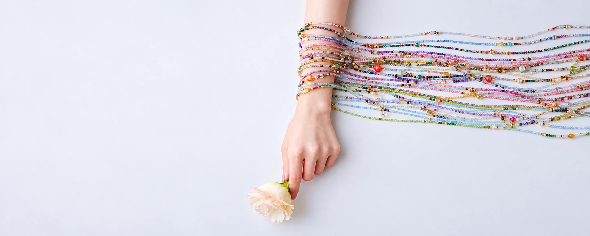 Colorful fine crystal bead strands draped over a hand holding a pale flower